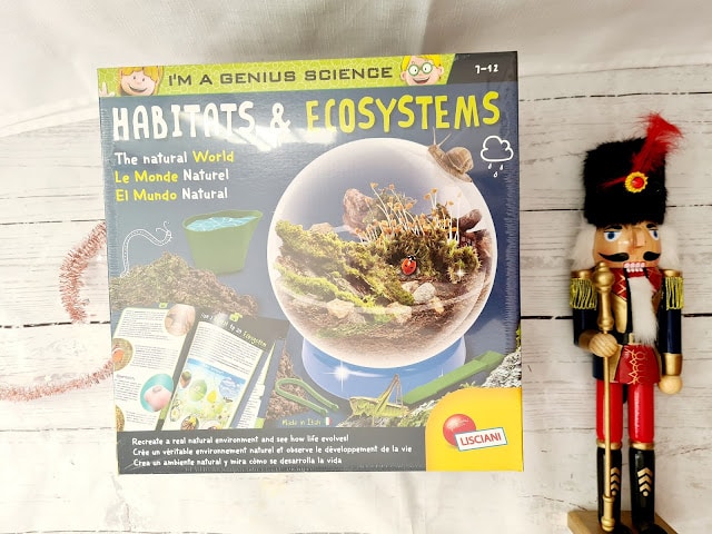 A "Habitats & Ecosystems" science kit box with colourful illustrations sits on a white wooden surface, making it a great addition to any Christmas Gift Guide for children. A decorative toy nutcracker in a red and black uniform stands nearby.