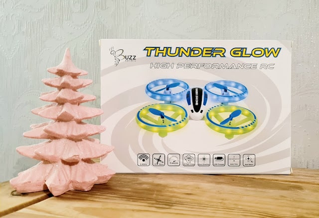 A pink decorative tree stands next to a Thunder Glow High Performance RC drone box, making it a perfect pick for any Christmas Gift Guide for Children, with images of glowing blue and yellow drones displayed on a wooden surface.