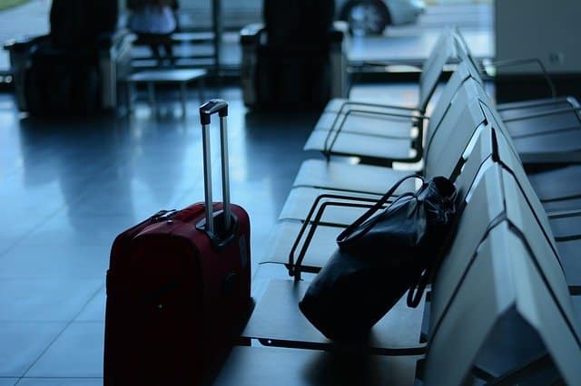 A red suitcase and a black bag rest on empty chairs in an airport waiting area, sunlight streaming through large windows—inviting thoughts of travel and the best places to visit post lockdown.