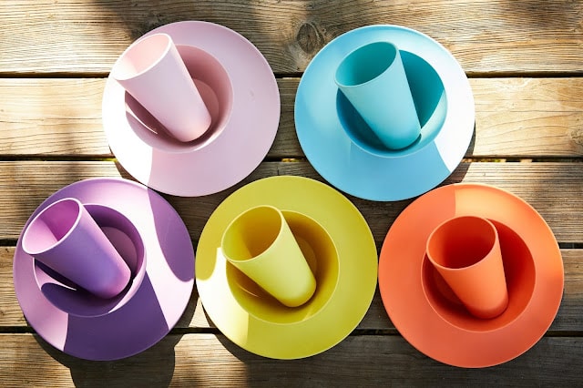 Five colourful sets of plastic plates and cups—pink, blue, purple, yellow, and orange—are arranged in a circle on a wooden surface, creating a bright and playful display perfect for UK bloggers hosting a Mother’s Day prize bundle.
