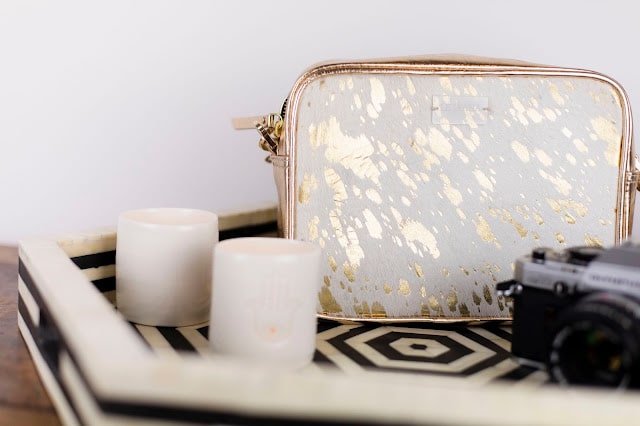 A small white and gold speckled bag sits on a black-and-white geometric tray alongside two white cups and a vintage camera—perfect for any UK Bloggers curating the ideal Mother’s Day gift collection.