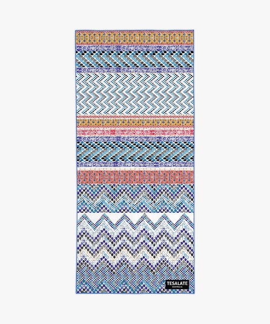 A rectangular towel with colourful geometric patterns, including zigzags and diamond shapes in blue, orange, purple, and white—perfect for a Mother’s Day prize bundle. The TESALATE logo is in the bottom right corner.