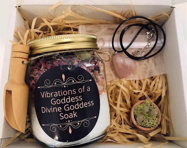 A Prize Bundle Giveaway gift box with straw filling featuring a "Vibrations of a Goddess Divine Goddess Soak" jar, wooden scoop, necklace with pink stone, and a tiny pot of green moss and crystals—perfect for Mother’s Day or UK Bloggers.