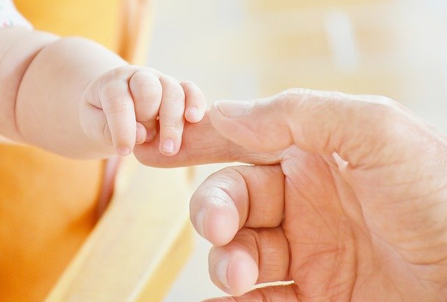 A baby's small hand gently grasps an adult's finger, symbolising trust and connection. This touching image beautifully captures one of the special ways to bond with children, highlighting tenderness and emotional closeness.