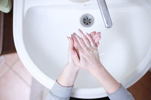 A person washing their hands with soap over a white basin, seen from above. Their hands are lathered with soap under a running tap—a simple act to help stop Covid and promote good hygiene.
