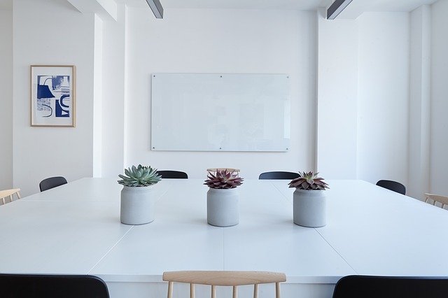 A minimalist conference room with a large white table, three potted succulents, black and wooden chairs, a blank whiteboard, and framed abstract art—perfect for an elegant looking home office or modern workspace.