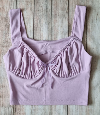 A lavender cropped vest top with wide straps and gathered, ruched fabric along the bust, perfect for capturing that summer vibe—displayed flat on a light wooden surface.