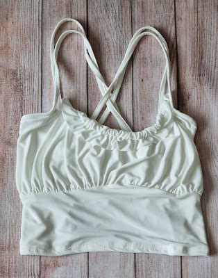 A Femmeluxe white cropped vest top with ruched detailing and thin, criss-crossed straps, laid flat on a wooden surface—perfect for channelling your summer groove.
