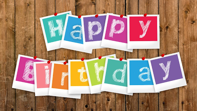 Colourful cards with letters spelling "Happy Birthday" are hung on a wooden wall. Each bright card brings a festive, cheerful vibe—perfect for a summer party celebration.