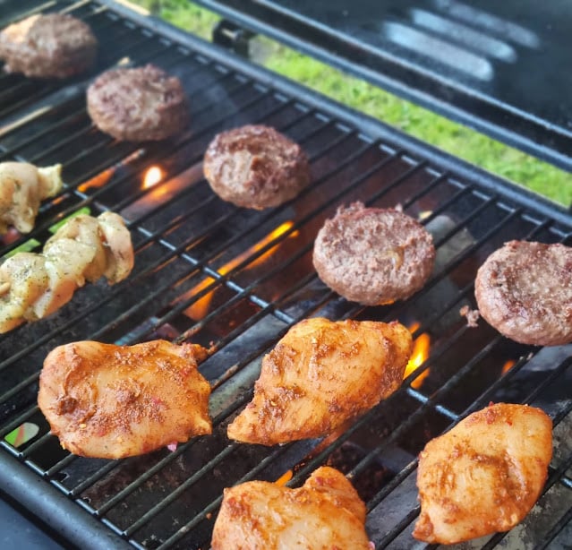 Chicken breasts, burger patties, and skewer pieces from Jack's Supermarket are being grilled on an outdoor barbeque over open flames, making for a perfect End of Term celebration on a sunny day.
