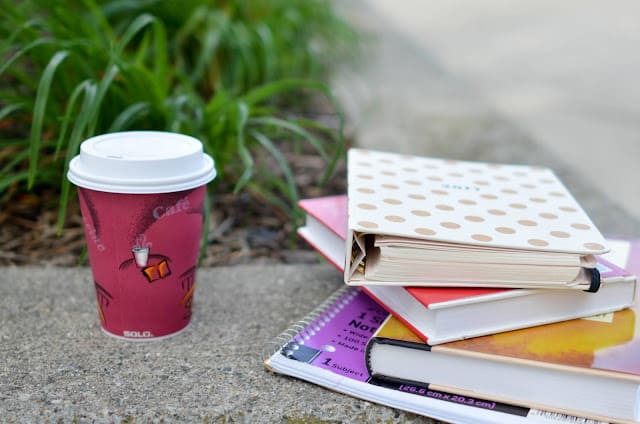 A pile of books on the ground next to a red disposable coffee cup