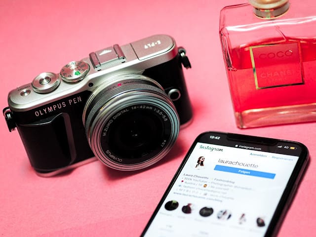 A camera sat next to a mobile phone and bottle of perfume