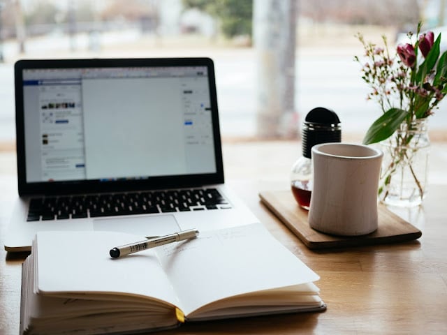 An open note book sat in front of a laptop and white coffee cup