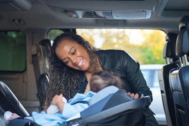 A woman placing her baby in a car seat in a car