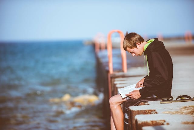 A young boy sat on a pier reading a booking