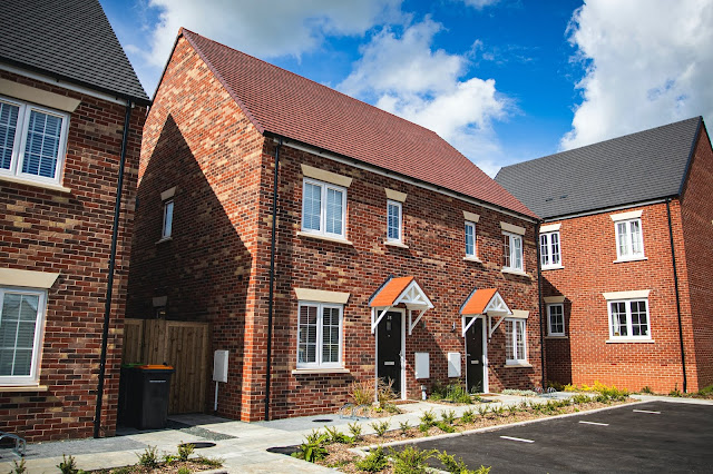 A row of modern red-brick semi-detached houses with white-framed windows and doors, small front gardens, and a paved drive under a blue sky—perfect for anyone searching for moving tips or things to consider before moving.