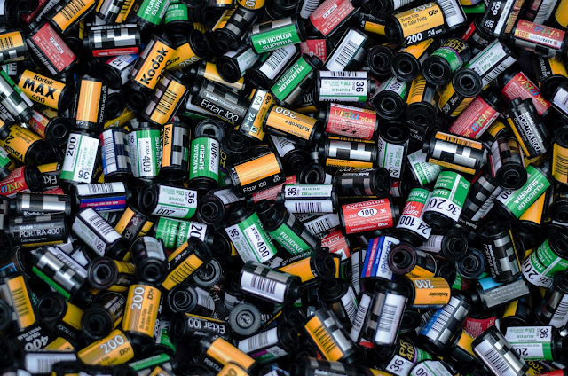 A large pile of assorted 35mm film canisters in various colours and brands, including Kodak and Fujifilm, tightly packed together—capturing how to make memories last through every snap.