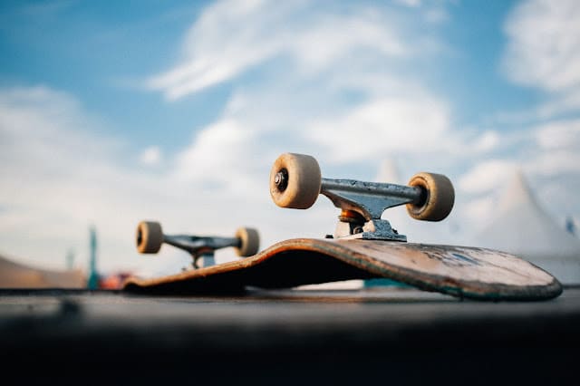 Close-up of a worn, broken skateboard lying upside down on a surface, with wheels visible against a blurred blue sky and white clouds—an ideal scene for lovers of outdoor gifts and fun presents.