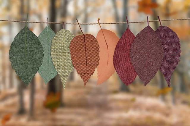 A number of fabric leaf cut outs on a string in front of trees
