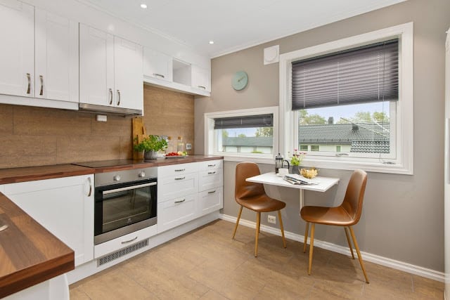A white kitchen with a small table and chairs on a wooden floor