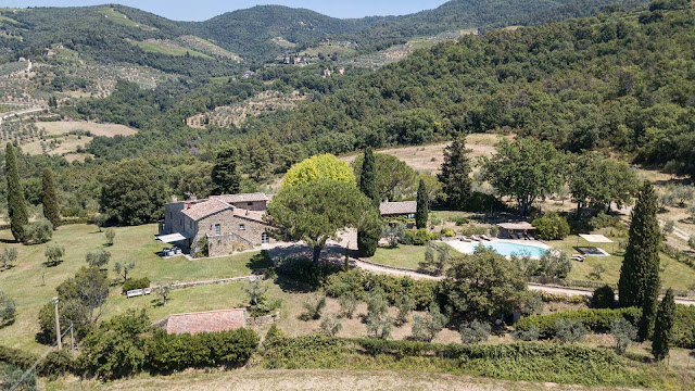 Aerial view of a rustic stone villa with a swimming pool, surrounded by trees and rolling hills—discover four reasons why Tuscany is a dreamy holiday destination in this idyllic rural countryside landscape.