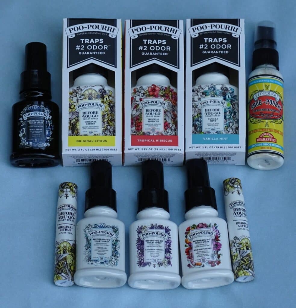 A collection of Poo-Pourri toilet sprays in various scents, including Original Citrus, Tropical Hibiscus, and Vanilla Mint, displayed in bottles, boxes, and travel-sized Poo-Pourri sprays on a light blue surface.