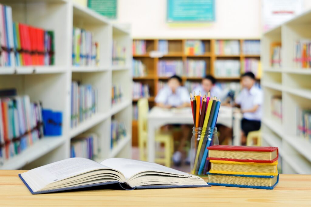 a textbook and other school items sat on a desk with a small group of children in the background