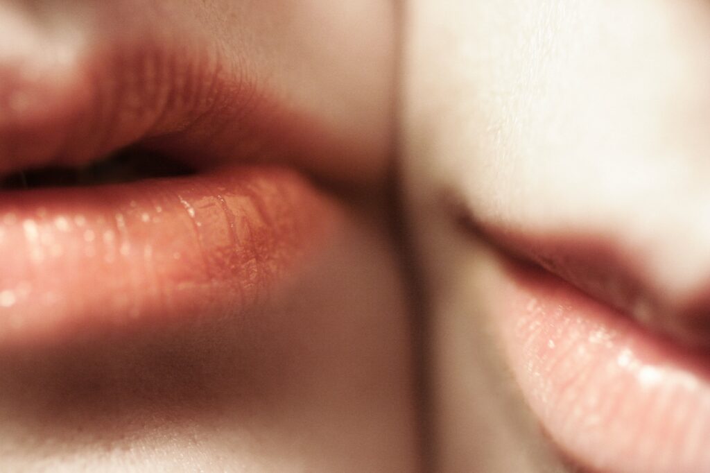 Close-up of two people’s lips, both slightly parted and softly lit. The smooth, natural texture suggests they’re cared for with Blistex, adding to the gentle, intimate atmosphere created by their close proximity and soft focus.
