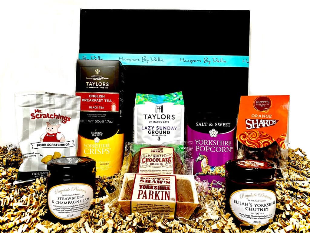 A black gift box labelled “Hampers By Delia,” surrounded by British snacks, including crisps, popcorn, chocolate, biscuits, and more—the perfect Yorkshire Lazy Sunday Treats Hamper.