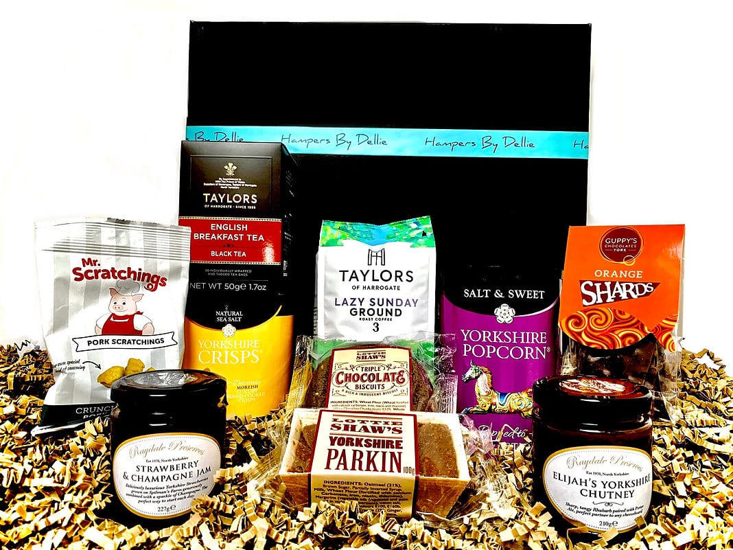 A black gift box labelled “Hampers By Delia,” surrounded by British snacks, including crisps, popcorn, chocolate, biscuits, and more—the perfect Yorkshire Lazy Sunday Treats Hamper.