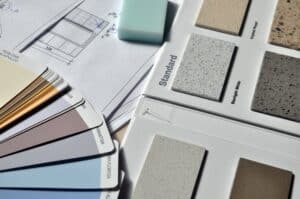 A close-up of architectural plans, colour swatches, worktop samples, and a light blue rubber arranged on a desk—perfect for brainstorming how you should structure your first home renovation.