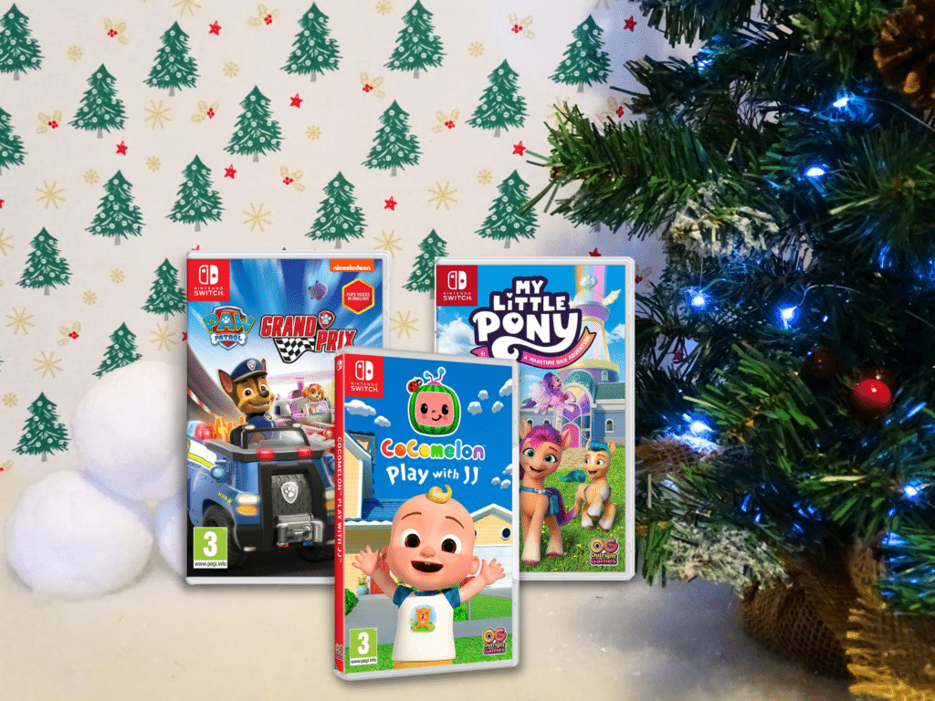 Three Nintendo Switch game cases—PAW Patrol Grand Prix, CoComelon Play with JJ, and My Little Pony—sit on a festive surface near a decorated Christmas tree, making them perfect Christmas Gift Ideas for Children 2022.