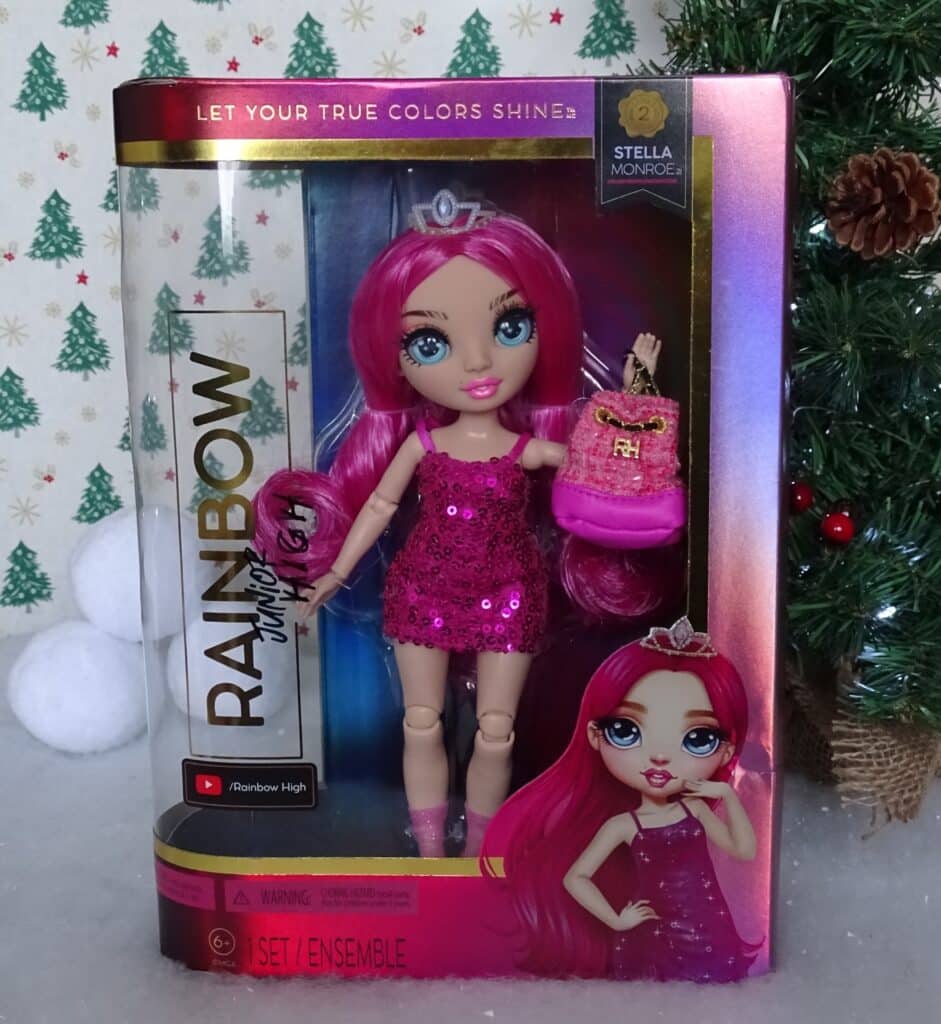 A Rainbow High fashion doll named Stella Monroe with long pink hair, wearing a sparkly pink dress, is displayed in a box featuring her illustration—a perfect addition to your Christmas Gift Ideas for Children 2022. A Christmas tree is visible in the background.