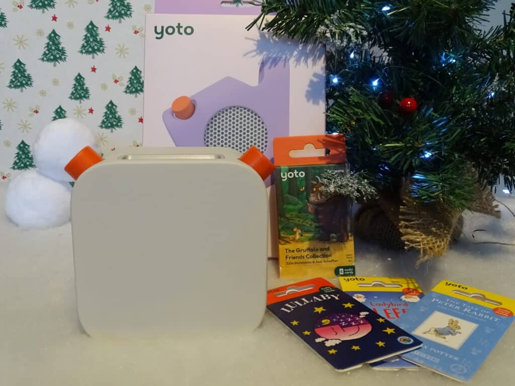 A Yoto player is displayed in front of its box, with several Yoto cards and a Christmas tree decorated with blue lights in the background—perfect for those seeking Christmas Gift Ideas for Children 2022 amid festive décor and wrapping paper.