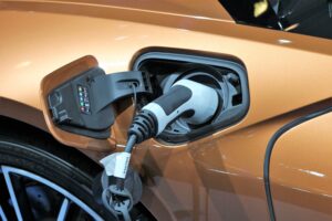 Close-up of an electric vehicle charging port with a plugged-in charger on a bronze-coloured car, highlighting modern options when deciding which car fuel type to choose in 2022. The charging flap is open, showing indicator lights and part of the rear wheel.