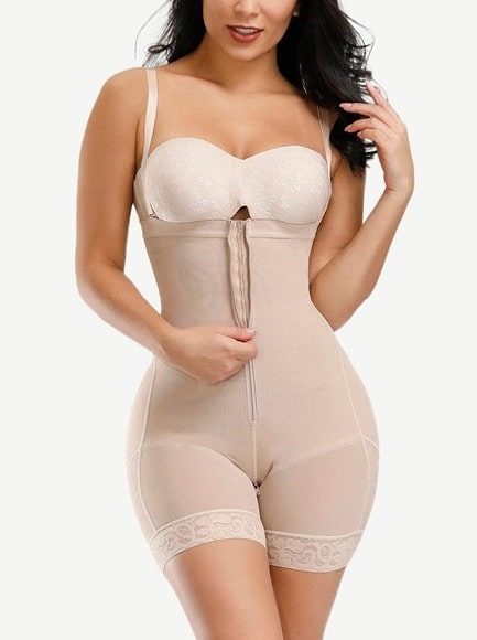 A woman wearing a nude-coloured shapewear bodysuit with adjustable straps, a front zip fastening, and lace trim on the thigh-length legs—one of the Fashion Investments Every Woman Must Have—stands against a white background.