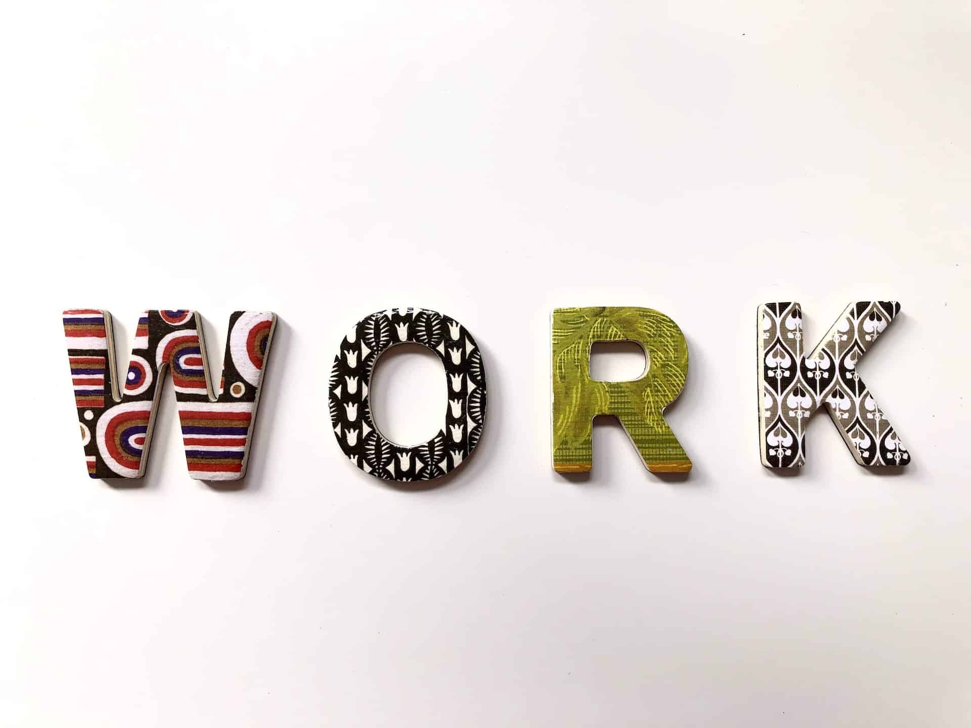 The word "WORK" spelt out in large, decorative letters, each with a different colourful pattern representing various professions, placed on a plain white background.