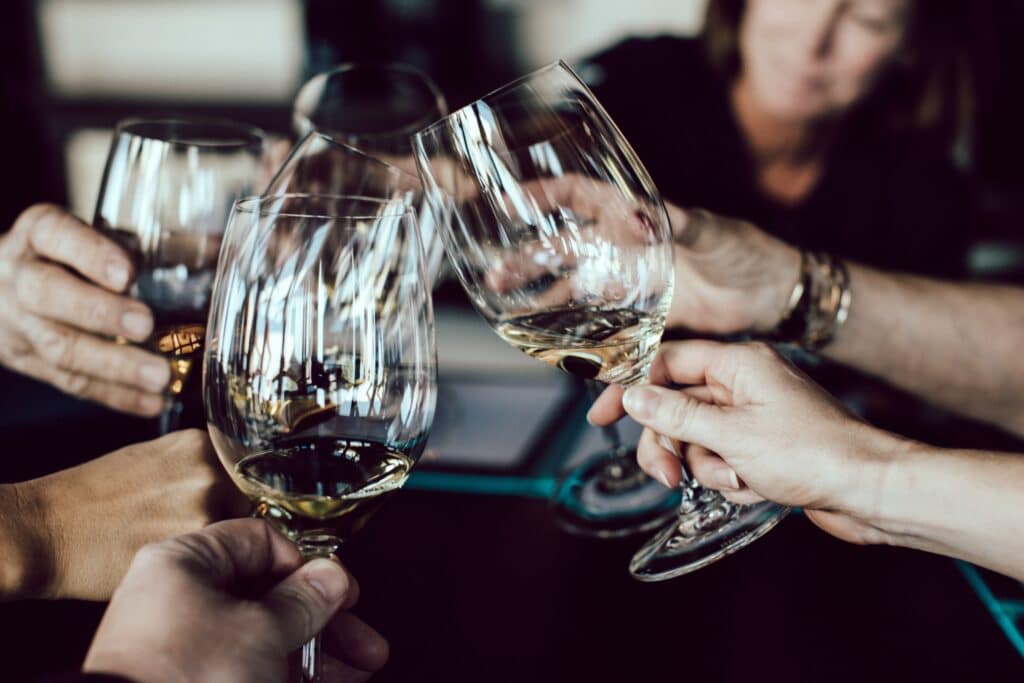 Five people clinking wine glasses together in a toast, celebrating with white and amber wine. The softly blurred background highlights the festive spirit—perfect for one of the 5 Celebrations You Should Hire an Irish Pub Venue For.