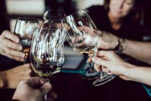 Five people clinking wine glasses together in a toast, celebrating with white and amber wine. The softly blurred background highlights the festive spirit—perfect for one of the 5 Celebrations You Should Hire an Irish Pub Venue For.