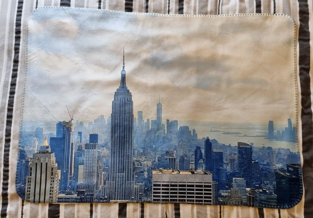 A rectangular mat with a printed image of the New York City skyline, featuring the Empire State Building at its centre, lies on a striped fabric background—showing how personalised gifts make the perfect present for city lovers.