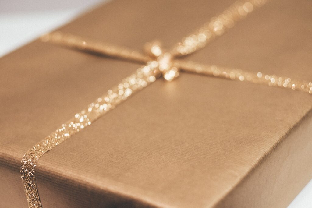 A close-up of a rectangular gift box wrapped in gold paper with a glittery ribbon tied in a simple bow, evoking the joy of giving. The soft focus highlights why personalised gifts make the perfect present for any festive occasion.