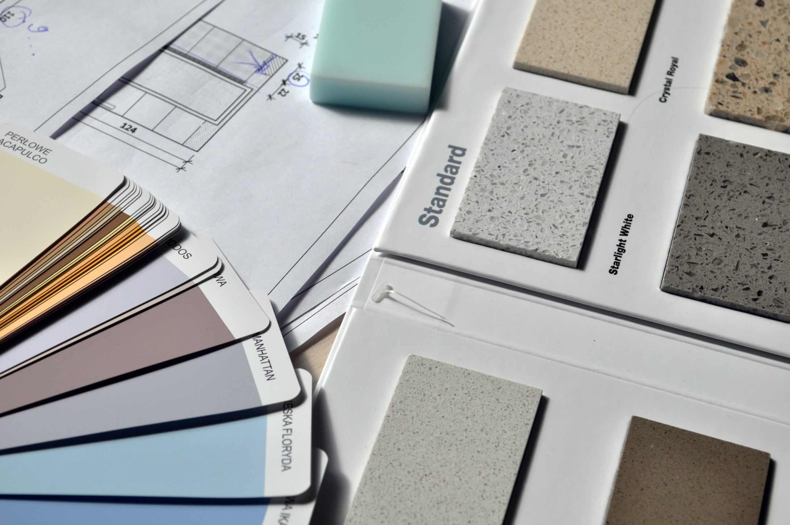 A selection of paint colour swatches, worktop material samples labelled "Standard," a rubber, and architectural drawings are arranged on a surface, illustrating the meticulous planning behind a successful home renovation project.