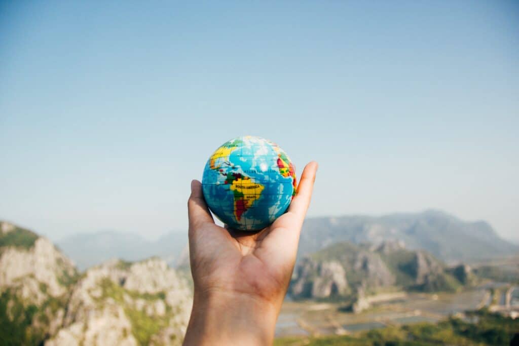 A hand holds a small globe against a clear blue sky, symbolising the excitement of going abroad for the first time—what you need to know before exploring new landscapes and distant mountains awaits.