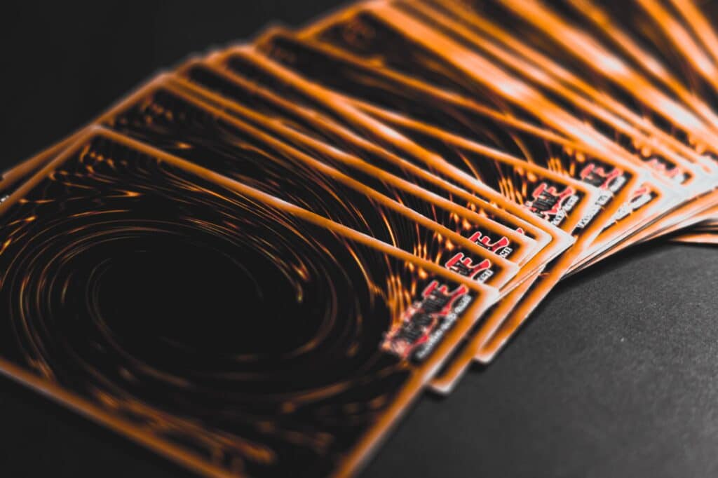 A fanned-out stack of Yu-Gi-Oh! trading cards displayed on a dark surface, showing their signature swirling orange and black card backs.