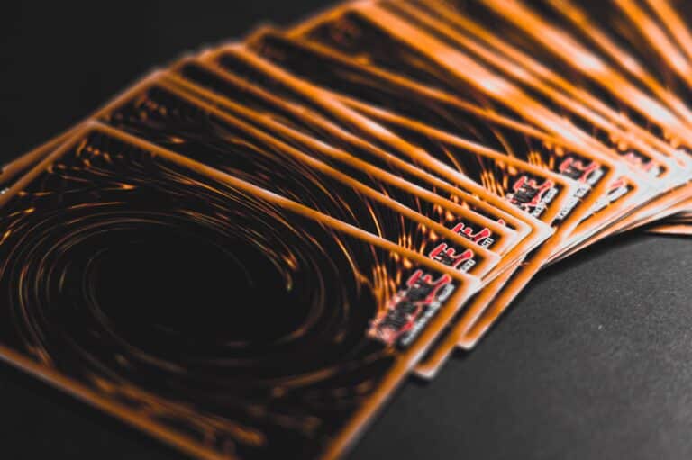 A fanned-out stack of Yu-Gi-Oh! trading cards displayed on a dark surface, showing their signature swirling orange and black card backs.