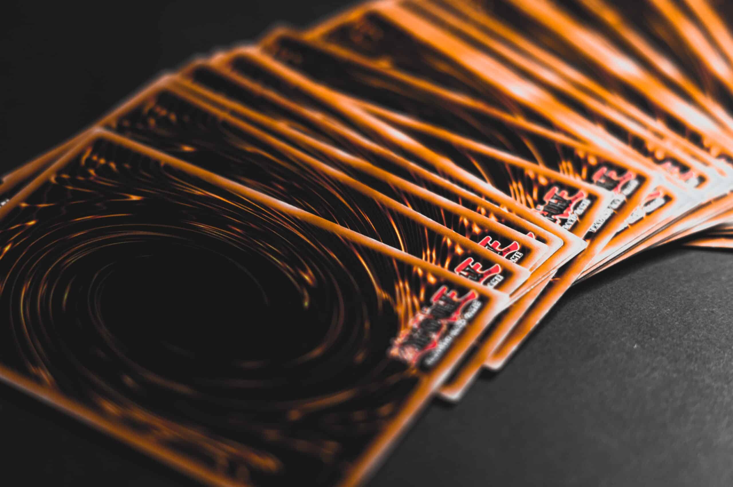 A fanned-out stack of Yu-Gi-Oh! trading cards displayed on a dark surface, showing their signature swirling orange and black card backs.