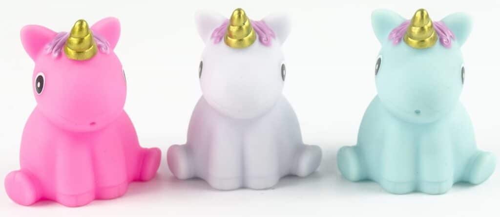 Three small toy unicorns are lined up side by side. If you must have Unicorn and Dinosaur toys, start with these adorable unicorns—pink, white, and light blue—with gold horns, big eyes, and small purple decorations near their ears.