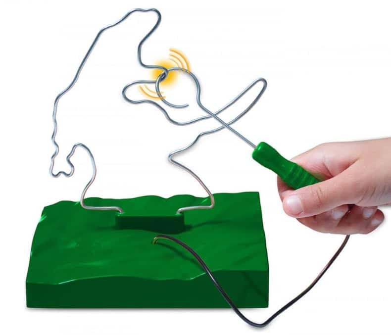 A hand is guiding a metal loop along a twisting wire track on a green base, similar to a steady-hand game. Unicorn and Dinosaur toys must be sitting nearby, while yellow lines indicate the loop has touched the wire, signalling a mistake.