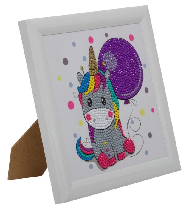 A framed picture of a cute, cartoon unicorn with a rainbow mane, gold horn, and purple balloon, created using colourful rhinestones on white with pastel dots—a must-have for fans of unicorn and dinosaur toys.