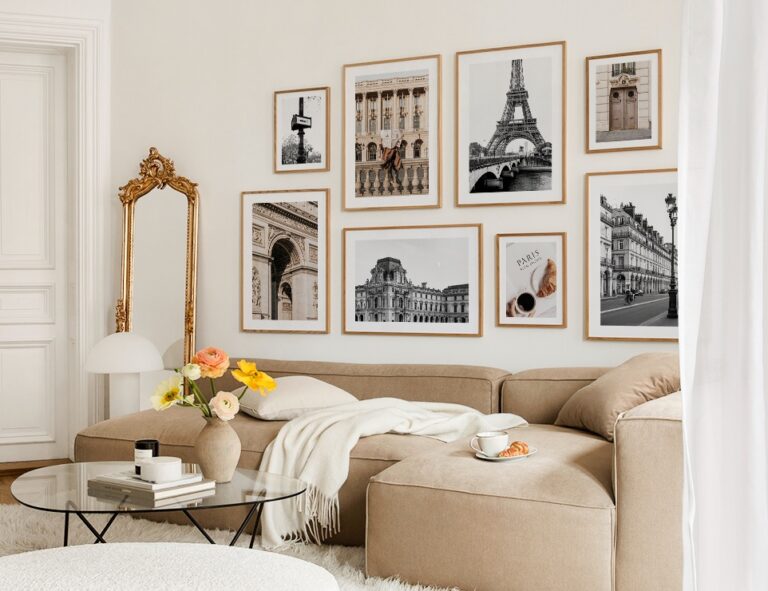 A modern living room with a beige corner sofa, glass coffee table, gold-framed mirror, and a gallery wall featuring framed photos of Paris landmarks—a perfect example of how to create a gallery wall at home.